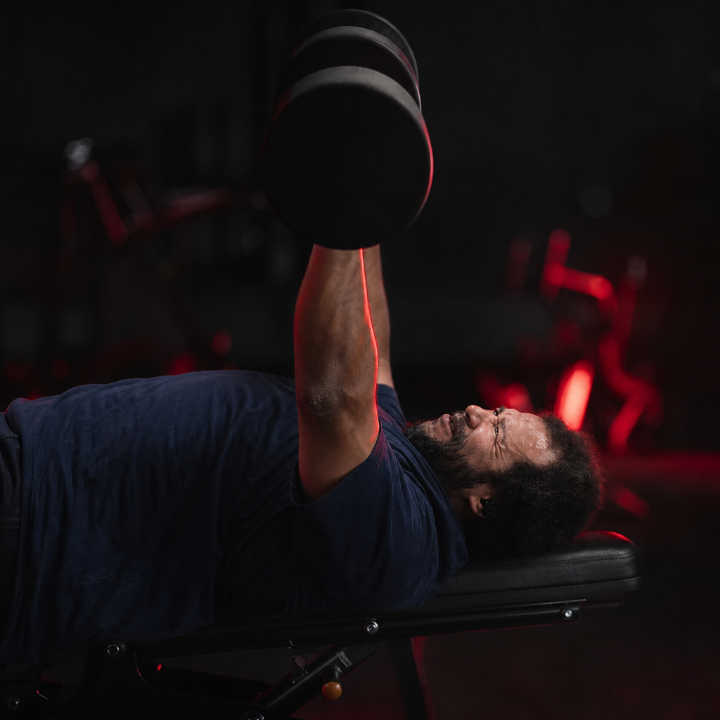 Man pressing dumbbells in a dark gym with crimson accent lighting